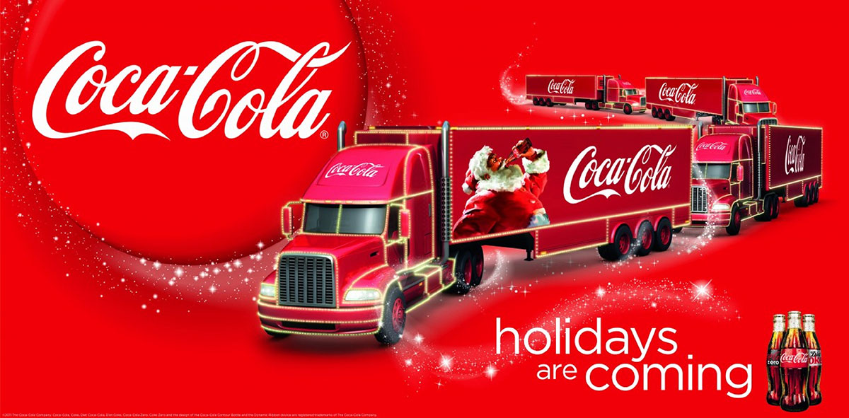 Coca-Cola Christmas trucks lit with fairy lights and a Santa graphic under the slogan holidays are coming on a red background