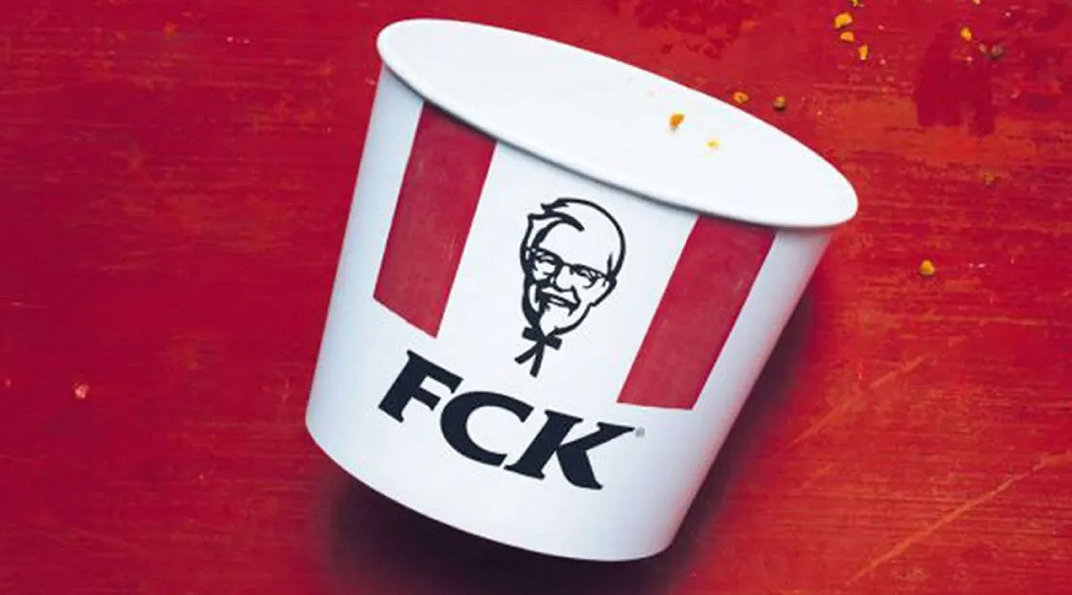 Empty KFC bucket with the letters rearranged to read FCK on a red background with crumbs